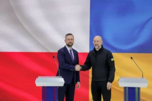 Польский министр обороны и украинский чиновник пожимают руки на фоне флагов двух стран