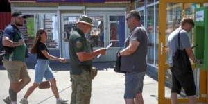 Військовий перевіряє документи чоловіка біля будівлі з перехожими