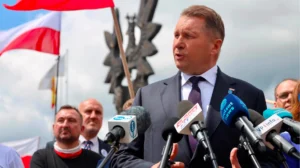 Пшемыслав Чарнек выступает перед микрофонами на фоне польских флагов