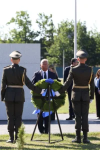 Два солдати встановлюють зелений вінок з блакитними стрічками біля чоловіка в костюмі