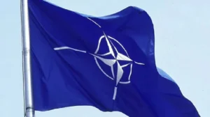 Синій прапор НАТО з білим емблемою майорить на флагштоку на тлі неба