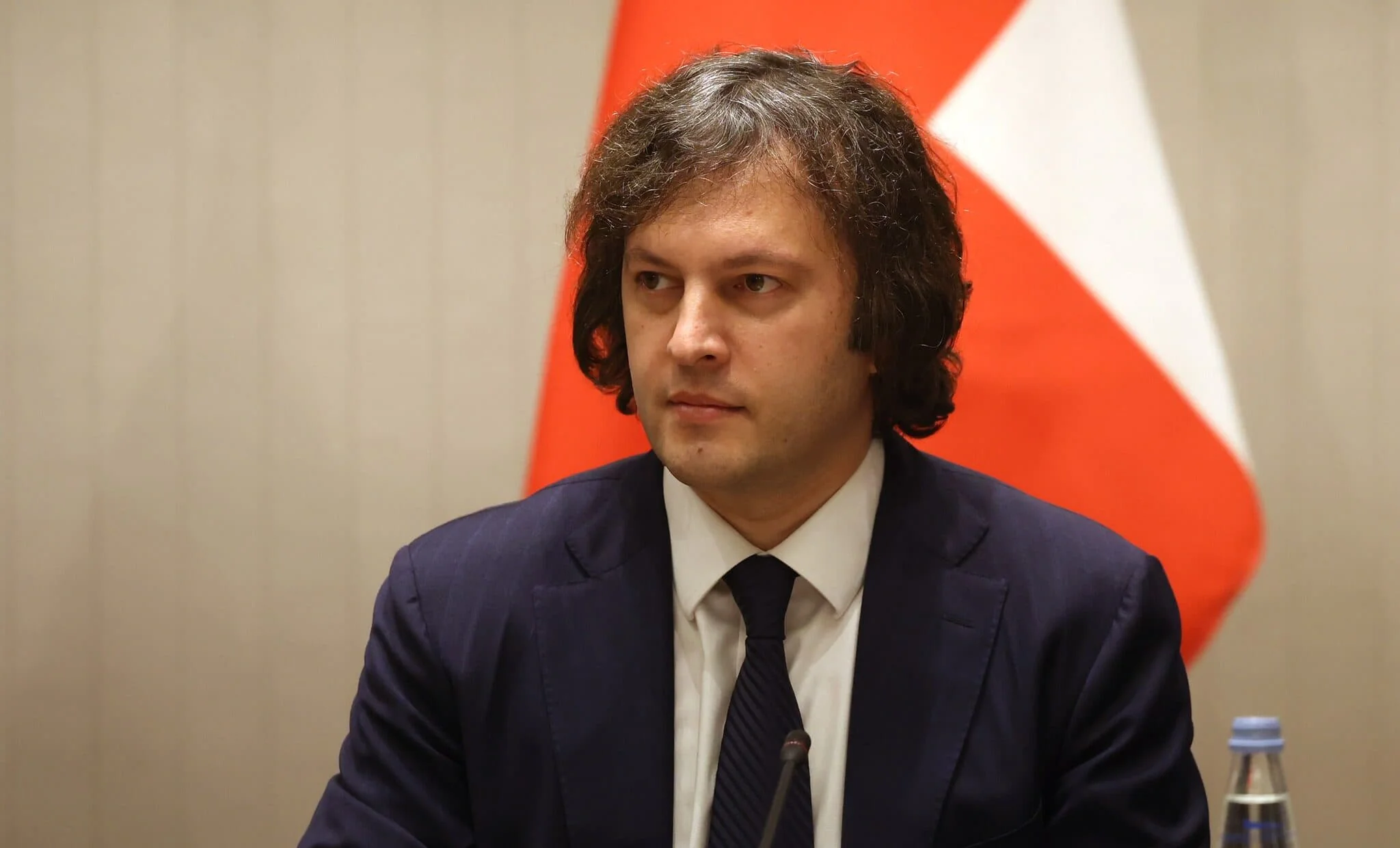 Іраклій Кобахідзе в синьому костюмі на тлі прапора Грузії