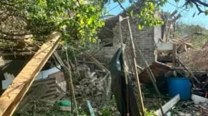Зруйнована цегляна будівля з уламками деревини та синьою бочкою після обстрілу