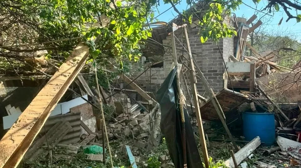 Зруйнована цегляна будівля з уламками деревини та синьою бочкою після обстрілу