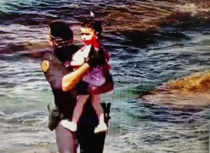 Поліцейський тримає маленьку дівчинку на руках у морських хвилях