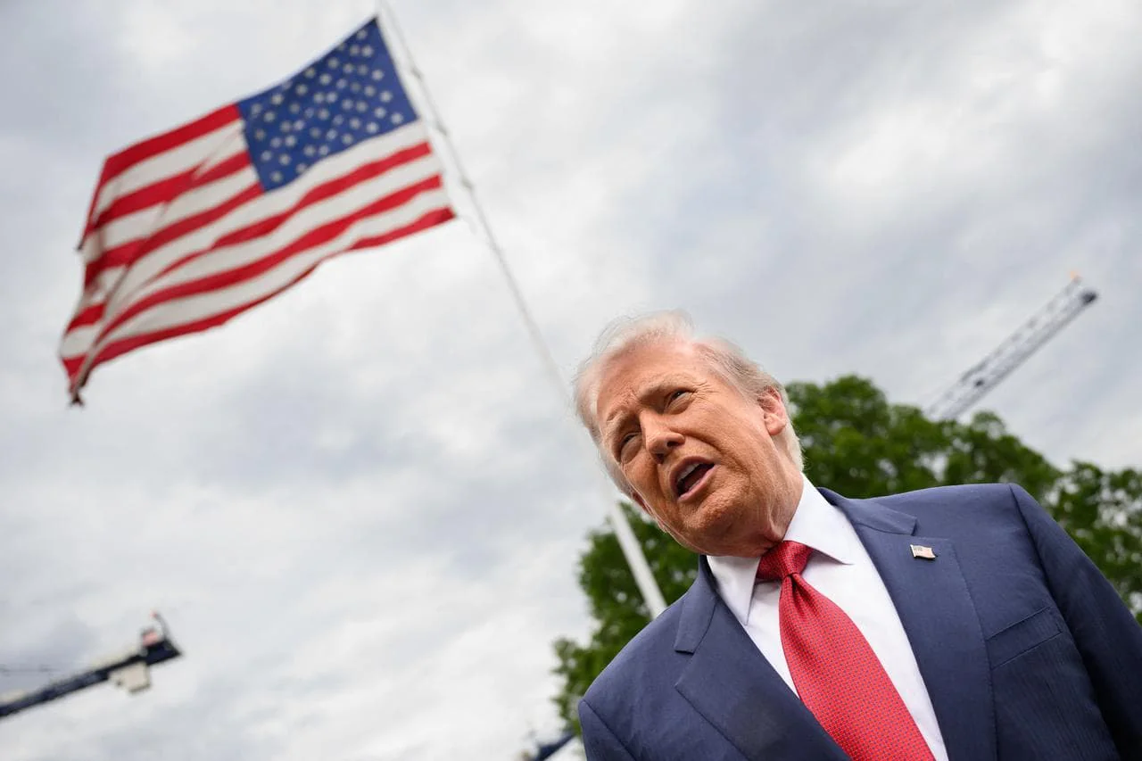 Дональд Трамп у синьому костюмі виступає на тлі прапора США