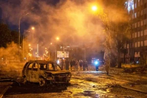 Обгорілий автомобіль на нічній вулиці серед диму та людей біля будівель