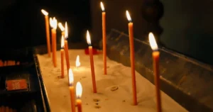 Запалені тонкі церковні свічки, встромлені в пісок на підсвічнику