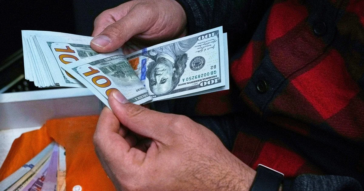 Чоловік у картатій сорочці перераховує пачку стодоларових купюр руками