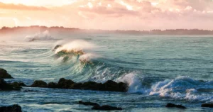 Морська хвиля з піною розбивається об скелі на тлі рожевого заходу сонця